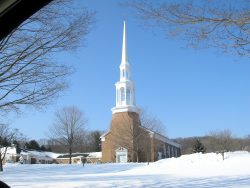 Distant view of church steeple, wintertime, snow on ground.